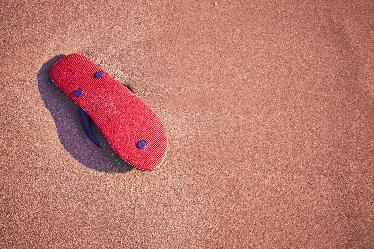 red rubber slipper upside down on top of some moist beach sand