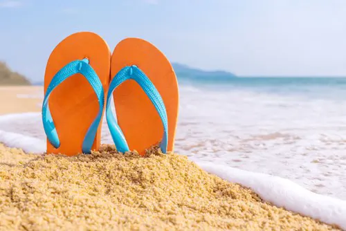 A pair of slippers stuck vertically into a mound of beach sand